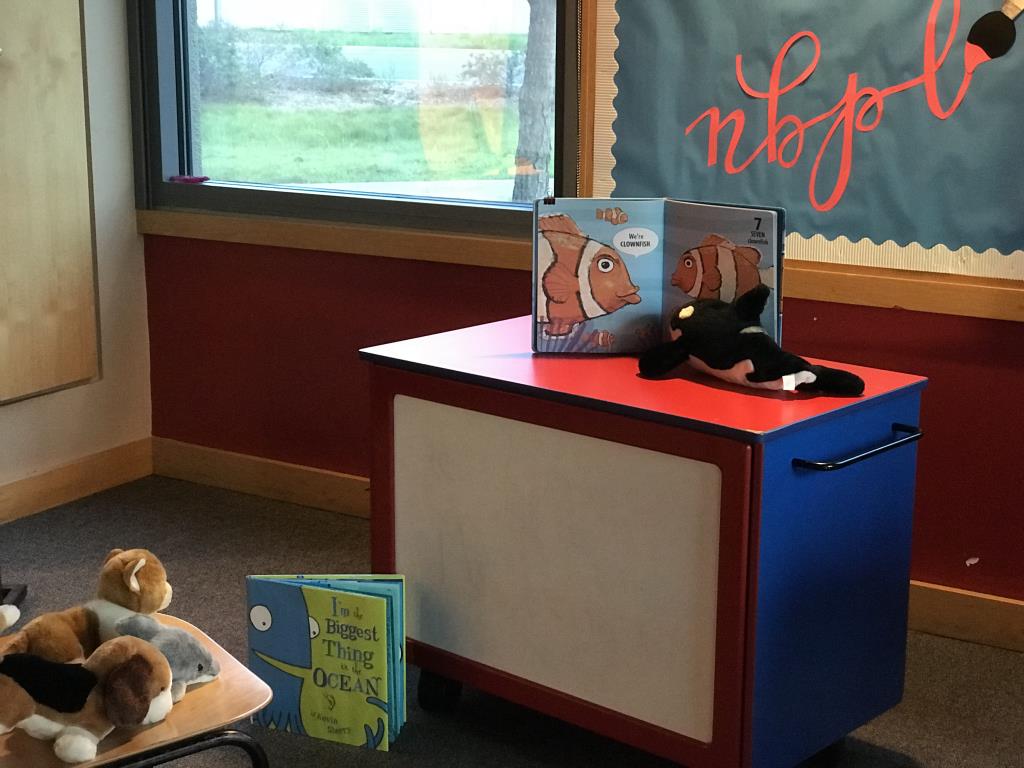 Stuffed animal Orca Whale reading a book about fish to stuffed animal dogs and cats